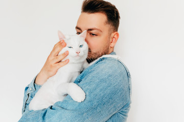 a young european man in denim shirt is holding and caressing a white cute cat with blue eyes. Love...