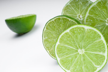 Various slices of green lemon over a white background.