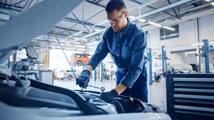 Professional Mechanic is Working on a Car in a Car Service. Repairman in Safety Glasses is Fixing the Engine on a Vehicle. Specialist Unscrews Bolts with a Ratchet. Modern Clean Workshop.