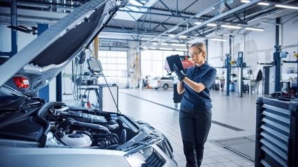 Female Mechanic Uses a Tablet Computer with an Augmented Reality Diagnostics Software. Specialist Inspecting the Car in Order to Find Broken Components Inside the Engine Bay. Modern Car Service. - Powered by Adobe