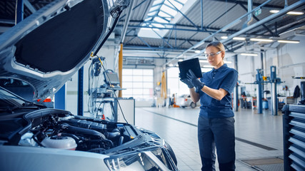 Female Mechanic Uses a Tablet Computer with an Augmented Reality Diagnostics Software. Specialist Inspecting the Car in Order to Find Broken Components Inside the Engine Bay. Modern Car Service.
