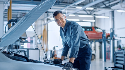 Handsome Professional Car Mechanic is Working on a Vehicle in a Service. Repairman Looks Happy...