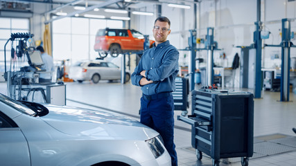 Handsome Car Mechanic is Posing in a Car Service. He Wears a Jeans Shirt and Safety Glasses. His...
