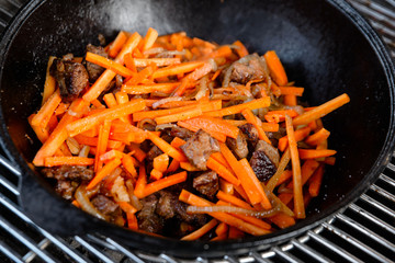 Pieces of lamb with onion are fried in boiling oil on the fire. As a stage in the preparation of traditional pilaf.step-by-step process of cooking pilaf in a cast iron cauldron on grill.