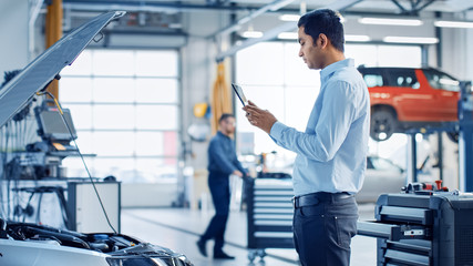 Car Service Manager Uses a Tablet Computer with an Augmented Reality Diagnostics Software. Specialist Inspecting the Car in Order to Find Broken Components Inside the Engine Bay.
