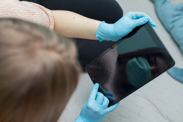 A high school graduate sitting on a bed with a tablet in hand in rubber gloves and a protective mask.
