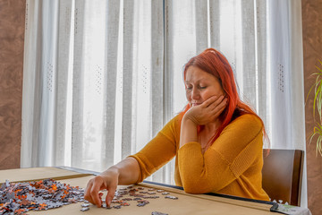 Beautiful redhead woman in a yellow sweater doing a puzzle in the living room at home