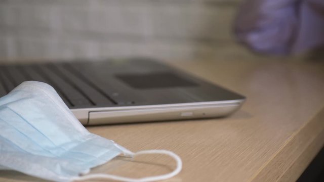 A freelancer working from home uses a computer to study online. Medical masks are on the table.