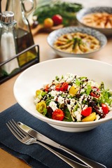 Mediterranean salad with cherry tomatoes, baby spinach, and authentic greek cheese.  Greek cuisine salad plating. Appetizer photography  on casual dine in table background.