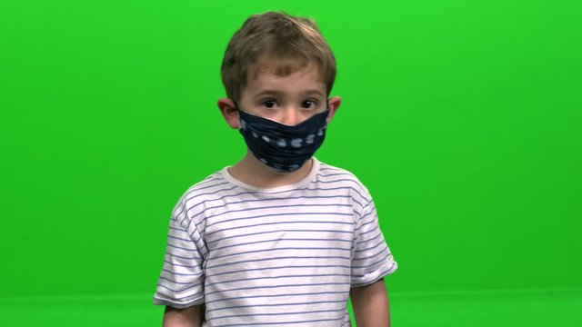 Little Boy with reusable cloth mask signs "Thumbs  up" over green screen.