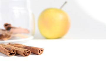 still life with food on the table are several sticks of cinnamon next to a jar of cinnamon and apples in the background on a white background