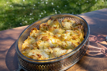 Baking tin of freshly oven baked italian specialty, the Rosette, small roses of lasagna pasta, york ham and bechamel sauce. Table and grass background, outdoor shot, natural light.