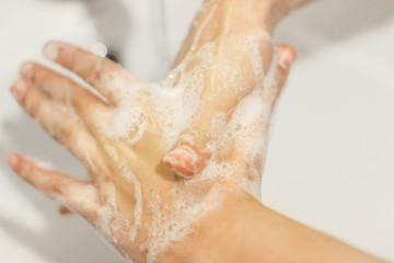 Fototapeta premium Rubbing big thumb, Washing hands with antibacterial soap in proper technique on background of flowing water in white bathroom. Prevention coronavirus. Cleaning and disinfecting