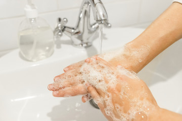 Wash your hands!  Washing hands with antibacterial soap in proper technique on background of flowing water in white bathroom. Prevention coronavirus. Cleaning and disinfecting