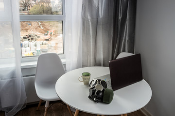 The Manager's workplace is at home, during quarantine. Business during the coronavirus pandemic. Laptop and coffee. Work during self-isolation. White kitchen table. Large window on the street.