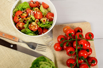 green lettuce with tomatoes, green olives and sunflower seeds in a white bowl