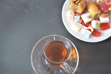 Tasty oriental sweets baklava, turkish delight on a plate on a dark black brown background and glasses of tea