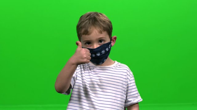 Little child with face mask demonstrates various hand gestures over green screen.