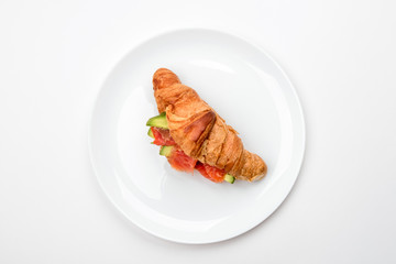Sandwich with salmon and avocado in a croissant on a white plate.