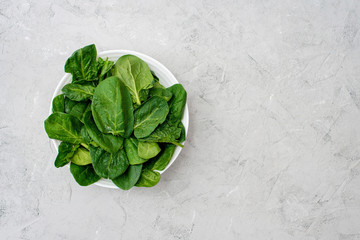 Clean food concept. Leaves of fresh organic spinach greens in a plate on a light background. Healthy detox spring-summer diet. Vegan Raw Food. Copy space.