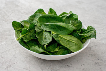 Clean food concept. Leaves of fresh organic spinach greens in a plate on a light background. Healthy detox spring-summer diet. Vegan Raw Food.