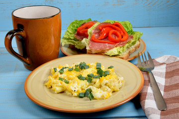 scrambled eggs with chives, a colorful sandwich and tea on an old blue table