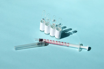 Drugs or vaccines in ampoules and an injection syringe on a light blue background.