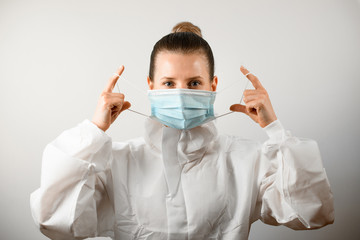 young woman in white protective suit gently puts medical mask