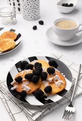 Pancakes with blackberries and coconut chips on white table.  Homemade gluten free breakfast