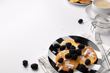 Pancakes with blackberries and coconut chips on white table.  Homemade gluten free breakfast