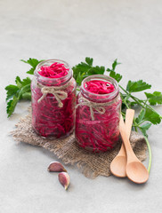 Cabbage marinated in beet juice with garlic and pepper in a jar on a light gray background in rustic style