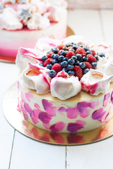 White and pink birhday cake with meringues and fresh berries, raspberries, strawberries and blueberries.