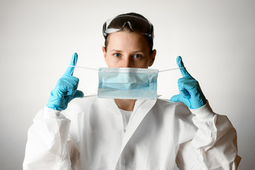 Naklejka premium Woman in white protective suit and gloves holds medical mask in her hands.
