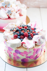 White and pink birhday cake with meringues and fresh berries, raspberries, strawberries and blueberries.