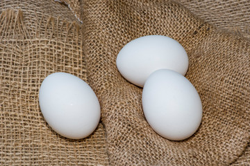 White chicken eggs wrapped in burlap next to a basket White eggs on burlap background