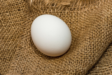 White chicken eggs wrapped in burlap next to a basket White eggs on burlap background