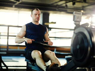 Fototapeta na wymiar Determined and middle aged man doing exercise on rope pull machine in gym