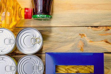 Products for donation are collected and lie on wooden table. Canned food, oil, jam, pasta. Top view, flat lay. Copy space for text. Close-up.
