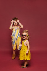 Cute little girl in a dress and sunglasses and little boy in a summer stylish overalls and sunglasses, isolated in full length at the pink background