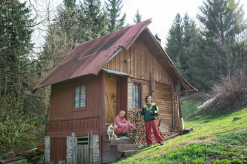 Two young women and their dog in front of an old cottage in the forest