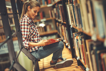 Young female student read and learns by the book shelf at the library.Reading a book.	
