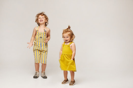Two cute stylish children, boy and girl in fashionable summer clothes posing on a beige background. Isolated in full length with copy space