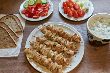 Grilled chicken skewers or kebabs made from chicken breasts and slices of onion, served with yogurth cucumber dip, slices of rustic bread and fresh chopped vegetables like sweet pepper and tomatoes.