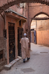 Fototapeta na wymiar Muslim man with djellaba and kufi strolling alley with shop on the street, blurred background