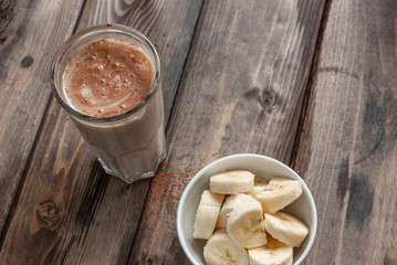 Banana smoothie with a transparent faceted glass in the background, next to a cup with a chopped banana. Healthy and tasty food.
