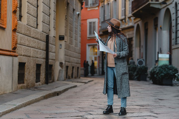 Young beautiful girl tourist stands on a road of cobblestones considering a map.