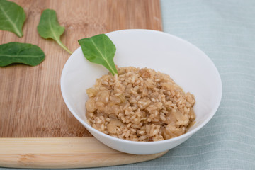 Stew of organic whole rice with onion pieces Inside a ceramic plate, on a wooden cutting board, next to spinach leaves,