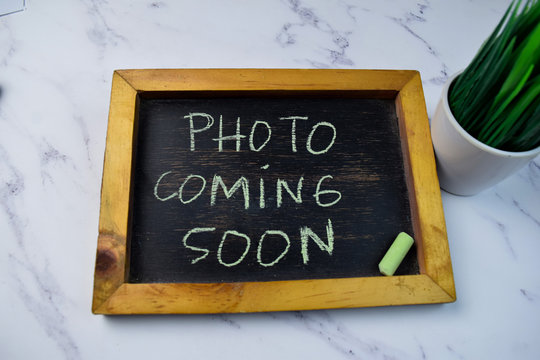 Photo Coming Soon write on a chalkboard isolated on wooden table.