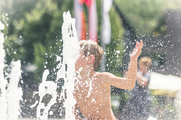 Little boy bathes in a city fountain. Boy having fun
