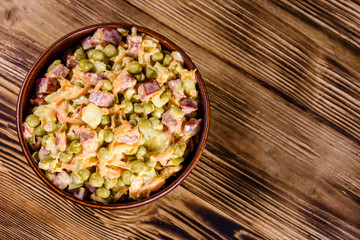 Salad with sausage, green pea, onion and carrot in glass bowl on wooden table. Top view